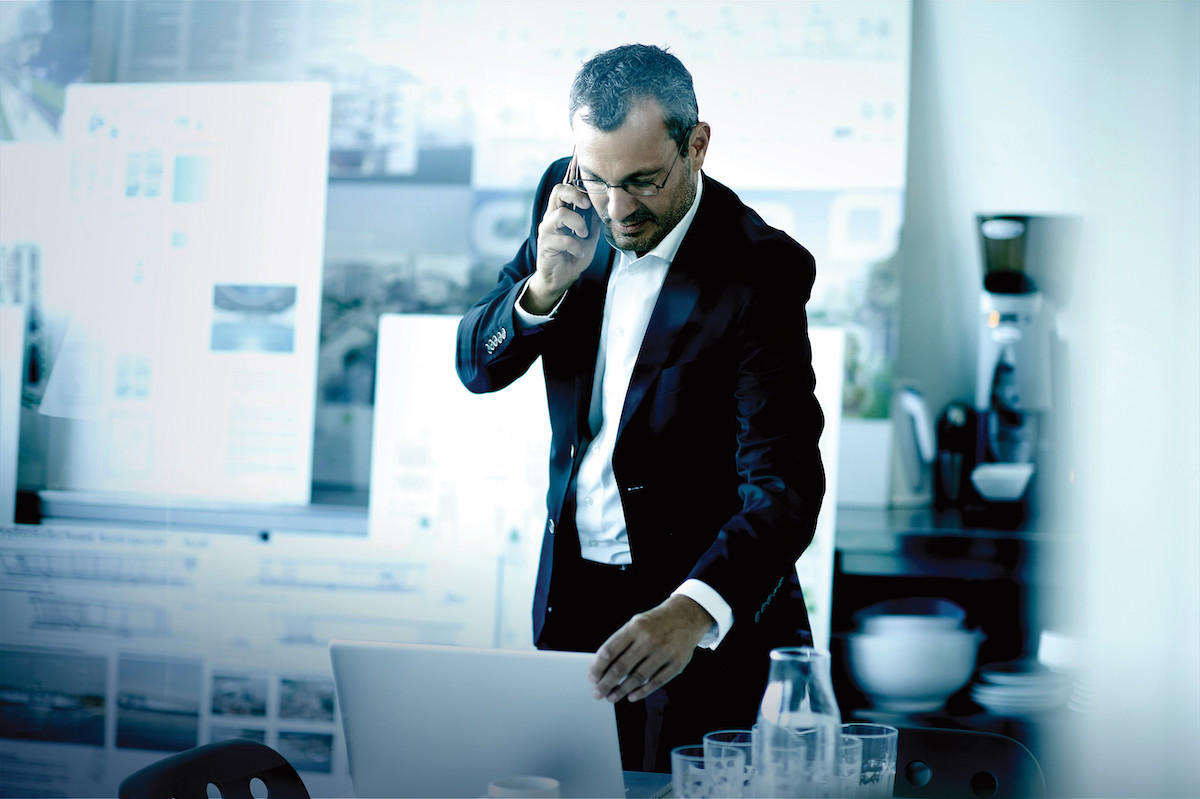 Business man chatting on smartphone whilst using office laptop